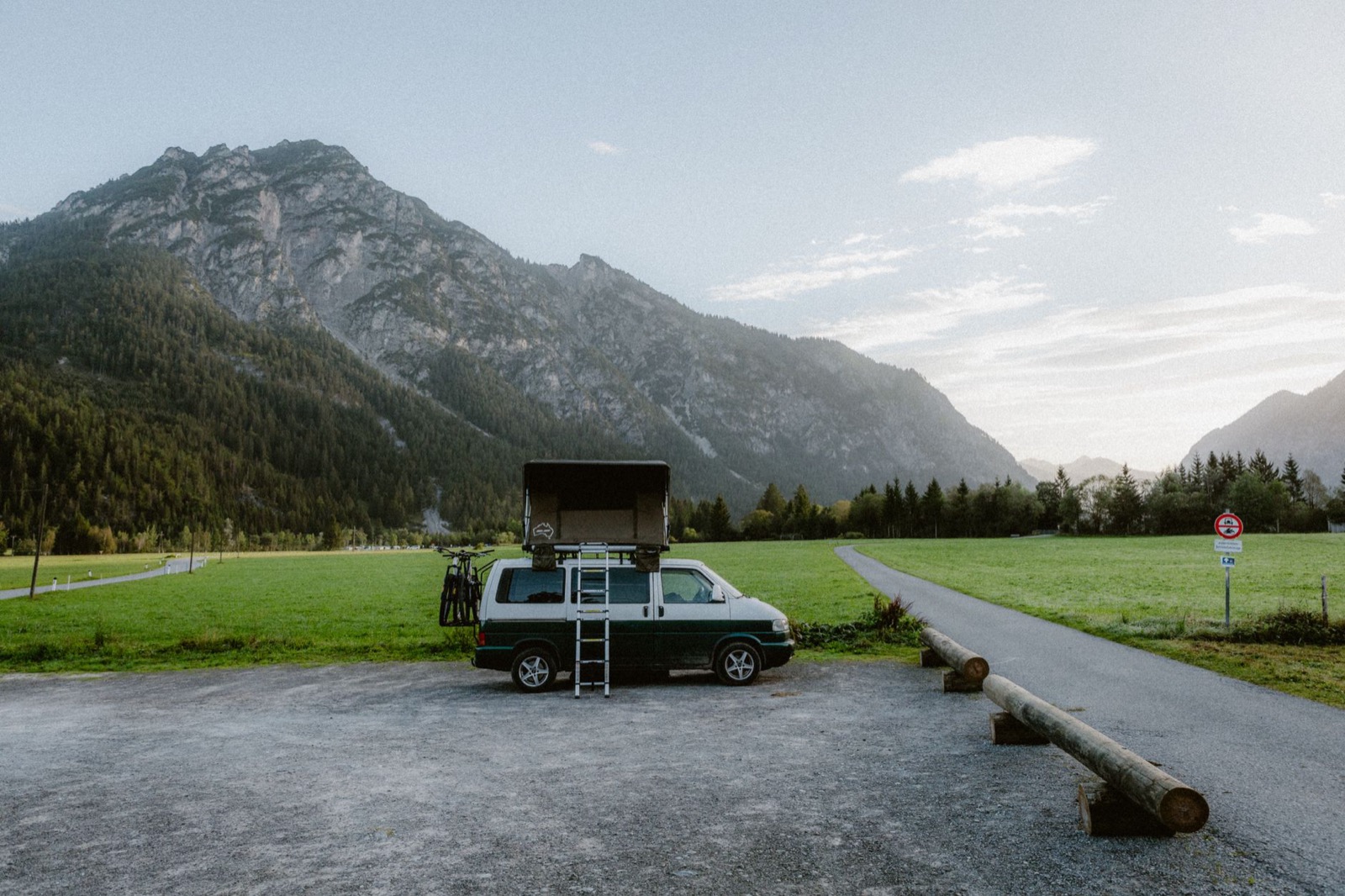 A van with its roof tent open and a ladder down, alone on a gravel car park in an alpine valley