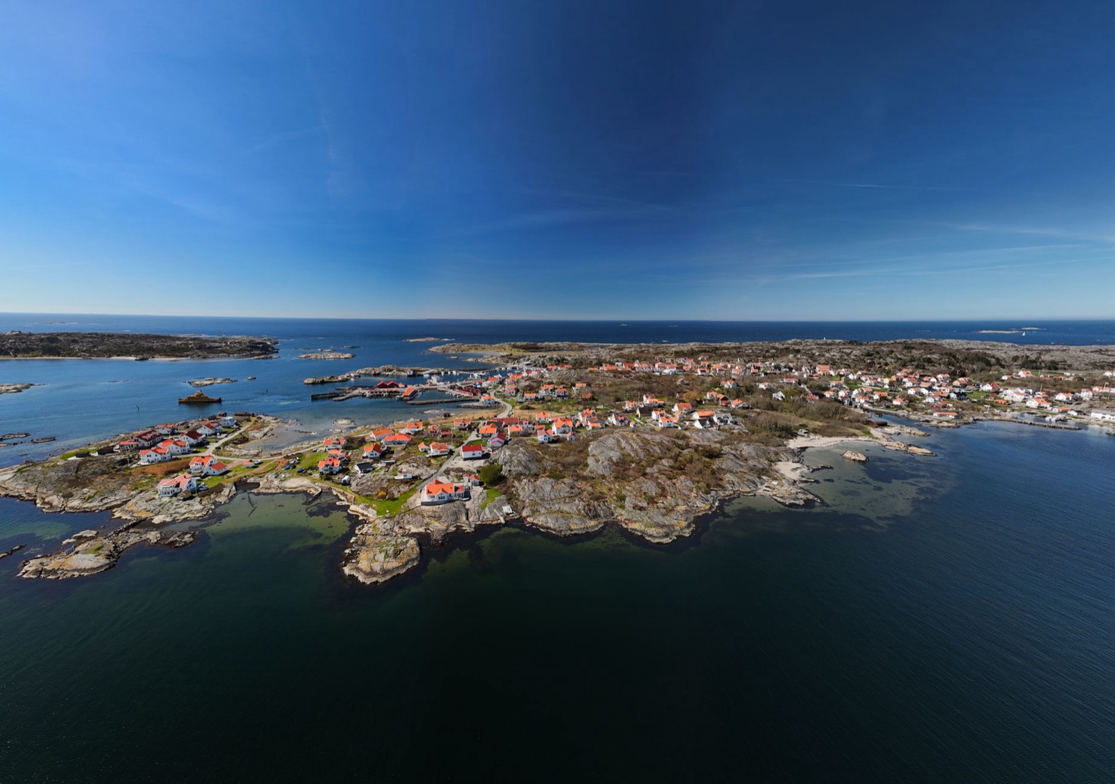 An aerial view of a village of red-roofed houses spread across a rocky archipelago headland