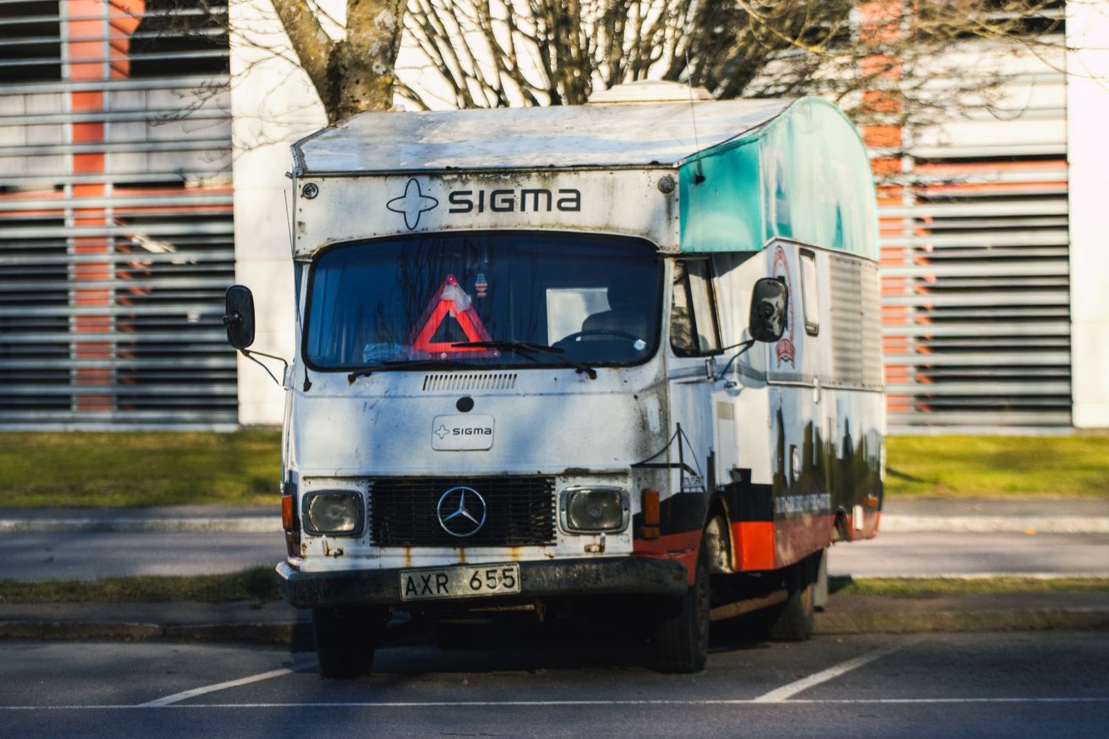 A battered box-body camper with Swedish plates standing in a marked parking bay