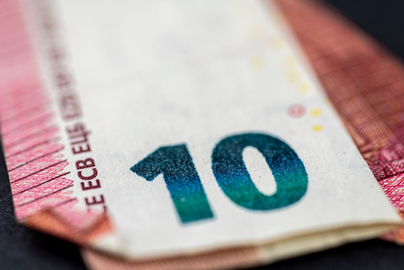 A ten euro note in close up, lying on a second note on a dark surface