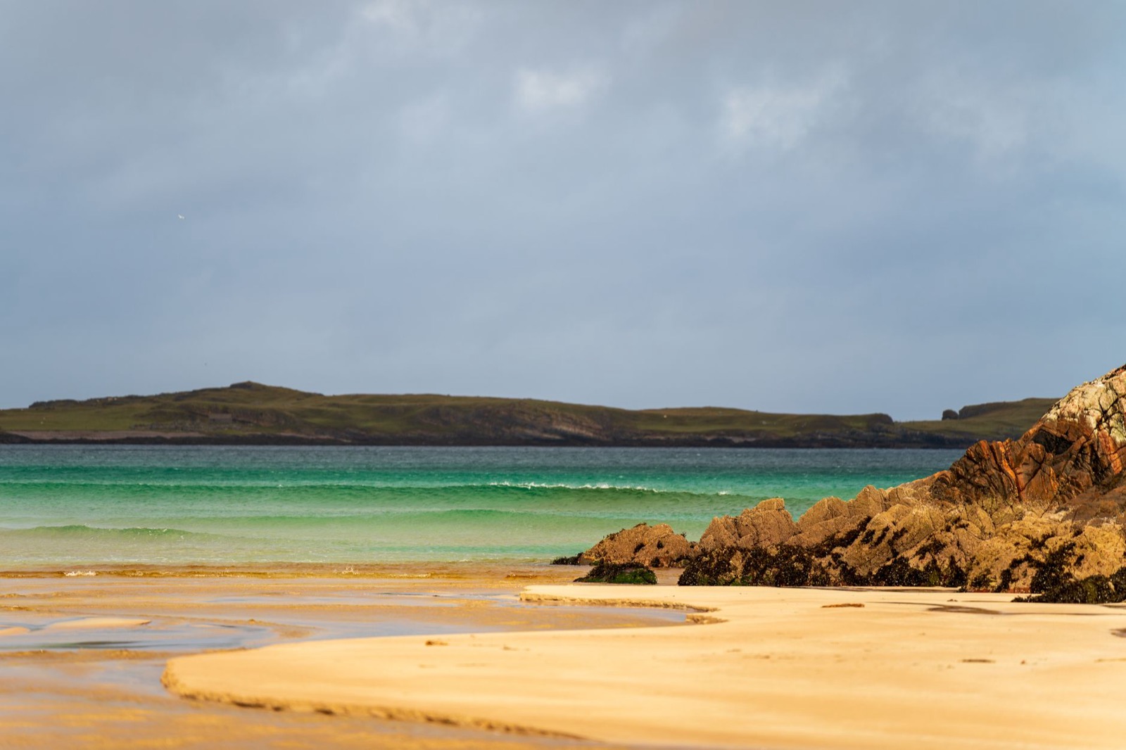A white sand beach with turquoise water and low machair grassland on a Hebridean island