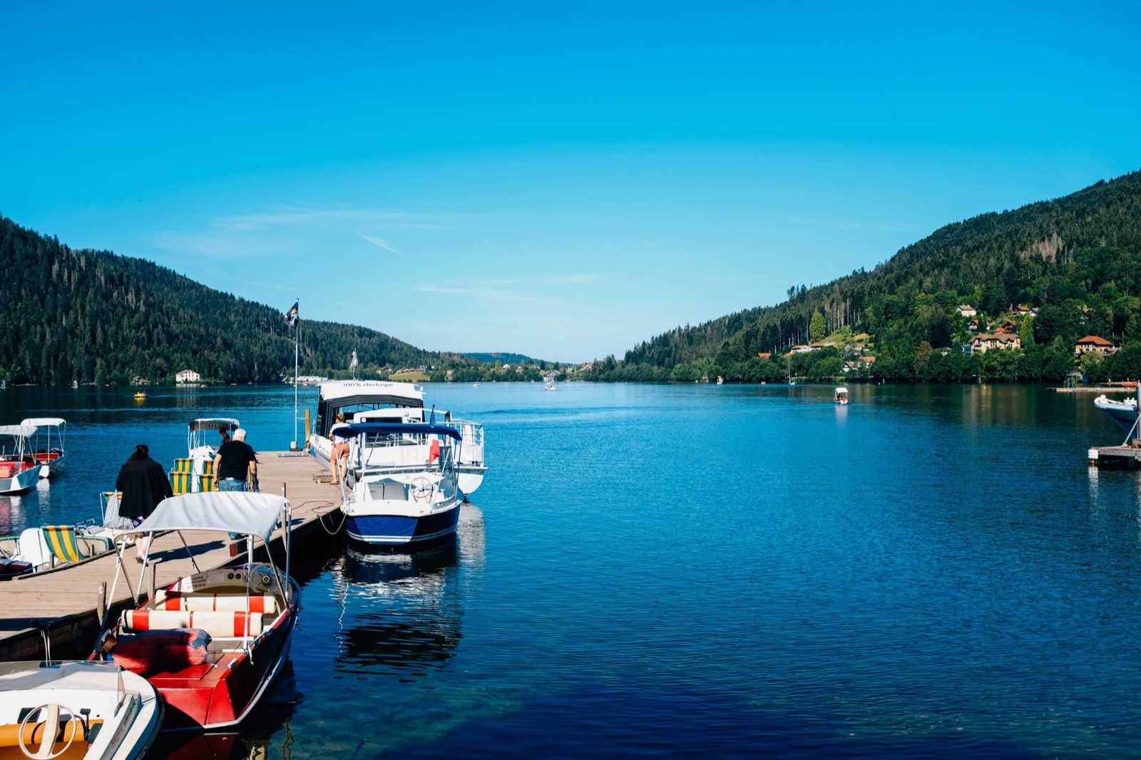 A lake below steep green fells with a stone jetty and moored rowing boats