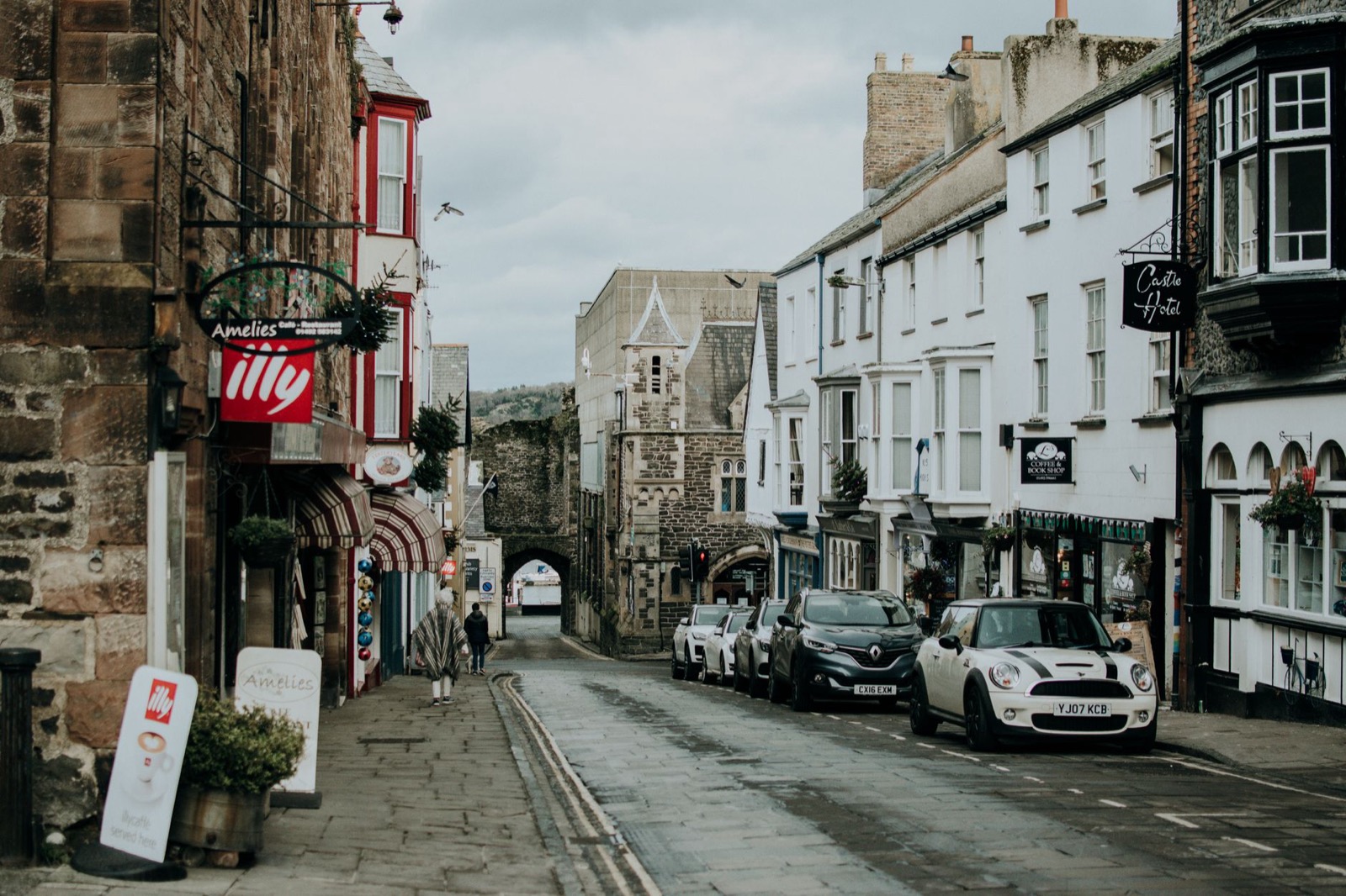 A stone-built British market town street with parked cars and shopfronts under grey sky